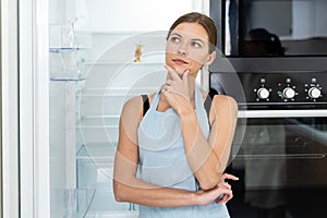 Young adult woman standing near refrigerator with apple