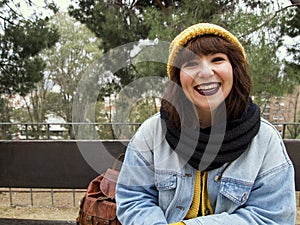 Young adult woman with yellow woolen cap sitting on a park bench smiling at the camera