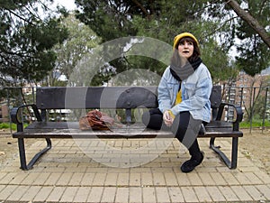 Young adult woman with yellow woolen cap sitting on a park bench thoughtful