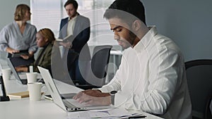 Young adults in businesswear talking and working on laptops at desk in office