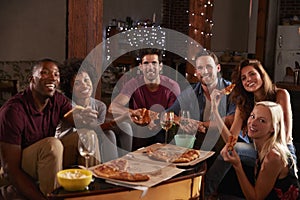 Young adults eating pizza at a party look to camera