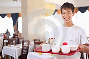 Young affable waiter keeps tray at restauran