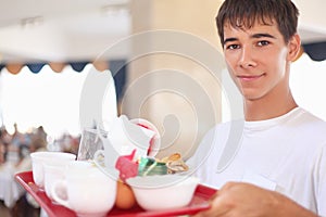 Young affable waiter keeps tray at restaurant