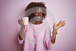 Young african afro woman holding cup of coffee standing over isolated pink background very happy and excited, winner expression