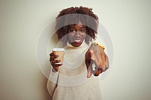 Young african afro woman holding cup of coffee standing over isolated white background pointing with finger to the camera and to