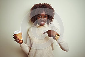 Young african afro woman holding cup of coffee standing over isolated white background with surprise face pointing finger to