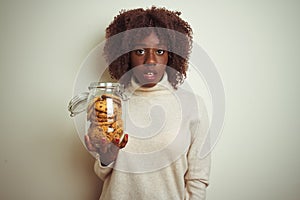 Young african afro woman holding jar of cookies standing over isolated white background scared in shock with a surprise face,