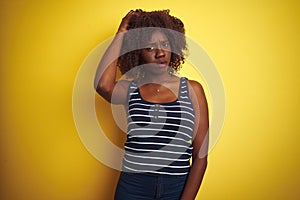 Young african afro woman wearing striped t-shirt over isolated yellow background confuse and wonder about question