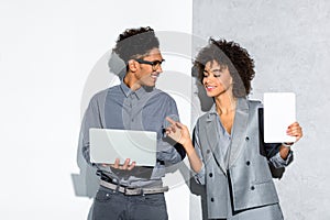 Young african amercian businessman with laptop and businesswoman with tablet in hand on grey and white