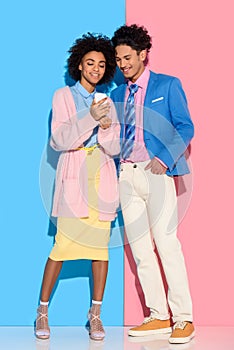 Young african amercian couple looking at phone screen on pink and blue