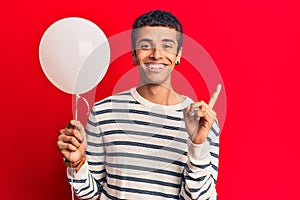 Young african amercian man holding balloon smiling happy pointing with hand and finger to the side