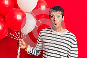Young african amercian man holding balloons scared and amazed with open mouth for surprise, disbelief face