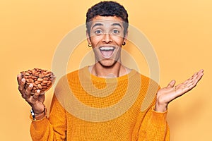 Young african amercian man holding bowl with almonds celebrating achievement with happy smile and winner expression with raised