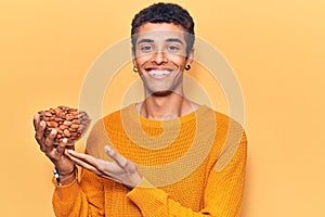 Young african amercian man holding bowl with almonds looking positive and happy standing and smiling with a confident smile