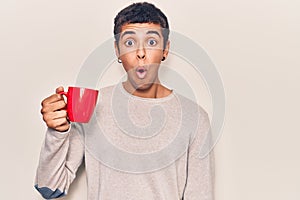 Young african amercian man holding coffee scared and amazed with open mouth for surprise, disbelief face