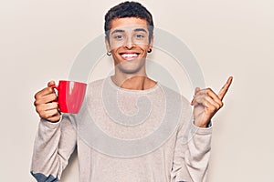 Young african amercian man holding coffee smiling happy pointing with hand and finger to the side