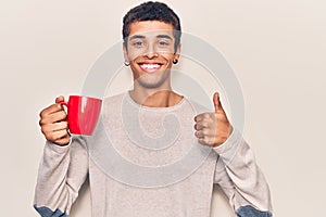 Young african amercian man holding coffee smiling happy and positive, thumb up doing excellent and approval sign