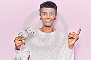 Young african amercian man holding dollars smiling happy pointing with hand and finger to the side