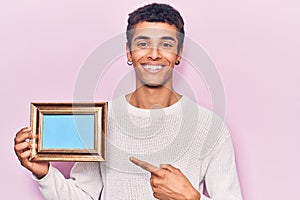 Young african amercian man holding empty frame smiling happy pointing with hand and finger