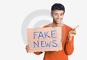 Young african amercian man holding fake news banner smiling happy pointing with hand and finger to the side