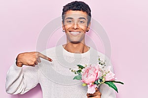 Young african amercian man holding flowers pointing finger to one self smiling happy and proud