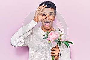 Young african amercian man holding flowers smiling happy doing ok sign with hand on eye looking through fingers