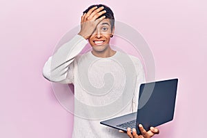 Young african amercian man holding laptop stressed and frustrated with hand on head, surprised and angry face