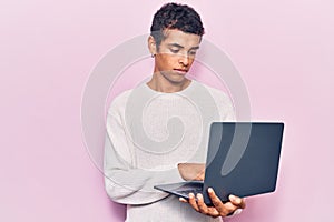 Young african amercian man holding laptop thinking attitude and sober expression looking self confident