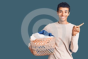 Young african amercian man holding laundry basket smiling happy pointing with hand and finger to the side