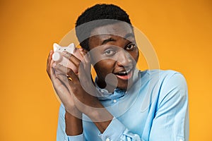 Young african amercian man holding piggy bank over yellow background