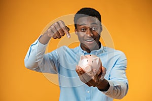 Young african amercian man holding piggy bank over yellow background