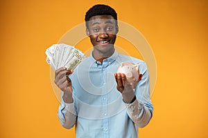 Young african amercian man holding piggy bank over yellow background