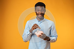 Young african amercian man holding piggy bank over yellow background
