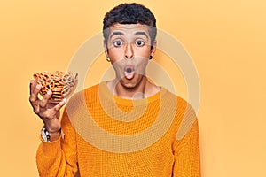 Young african amercian man holding pretzels scared and amazed with open mouth for surprise, disbelief face