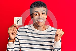 Young african amercian man holding question mark reminder screaming proud, celebrating victory and success very excited with