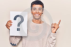 Young african amercian man holding question mark smiling happy pointing with hand and finger to the side