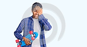 Young african amercian man holding skate stressed and frustrated with hand on head, surprised and angry face