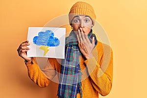 Young african amercian man holding thunder draw covering mouth with hand, shocked and afraid for mistake