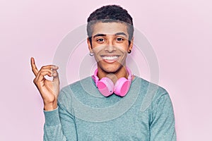 Young african amercian man listening to music using headphones smiling happy pointing with hand and finger to the side