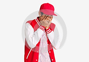 Young african amercian man wearing baseball uniform with sad expression covering face with hands while crying