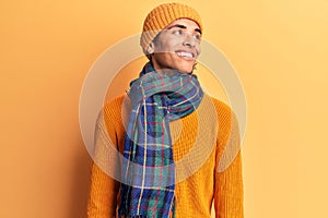 Young african amercian man wearing casual winter clothes looking away to side with smile on face, natural expression