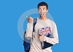 Young african amercian man wearing student backpack holding binder and uk flag pointing thumb up to the side smiling happy with