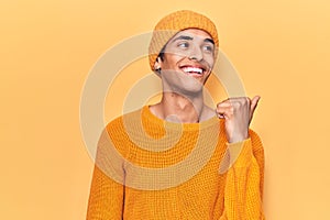 Young african amercian man wearing wool cap pointing thumb up to the side smiling happy with open mouth