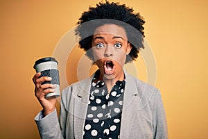Young African American afro businesswoman with curly hair drinking cup of coffee scared in shock with a surprise face, afraid and