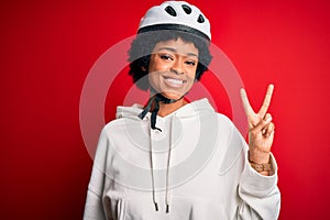 Young African American afro cyciling woman with curly hair wearing bike security helmet smiling with happy face winking at the