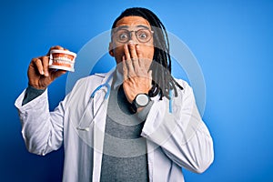 Young african american afro dentist doctor man wearing stethoscope holding teeth cover mouth with hand shocked with shame for