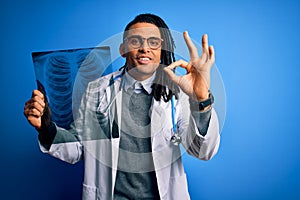 Young african american afro doctor man with dreadlocks holding chest lung xray doing ok sign with fingers, excellent symbol