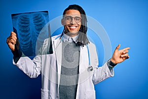 Young african american afro doctor man with dreadlocks holding chest lung xray very happy pointing with hand and finger to the