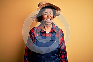 Young African American afro farmer woman with curly hair wearing apron and hat winking looking at the camera with sexy expression,