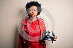 Young African American afro motorcyclist woman with curly hair holding motorcycle helmet puffing cheeks with funny face